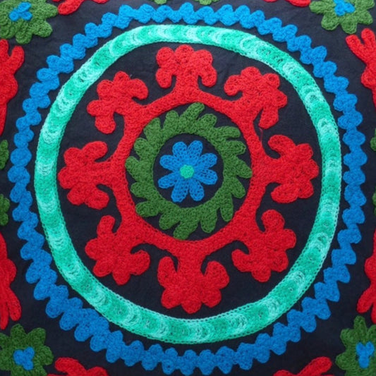 A colorful geometric patterned cushion cover with pom pom trim on a wooden chair.