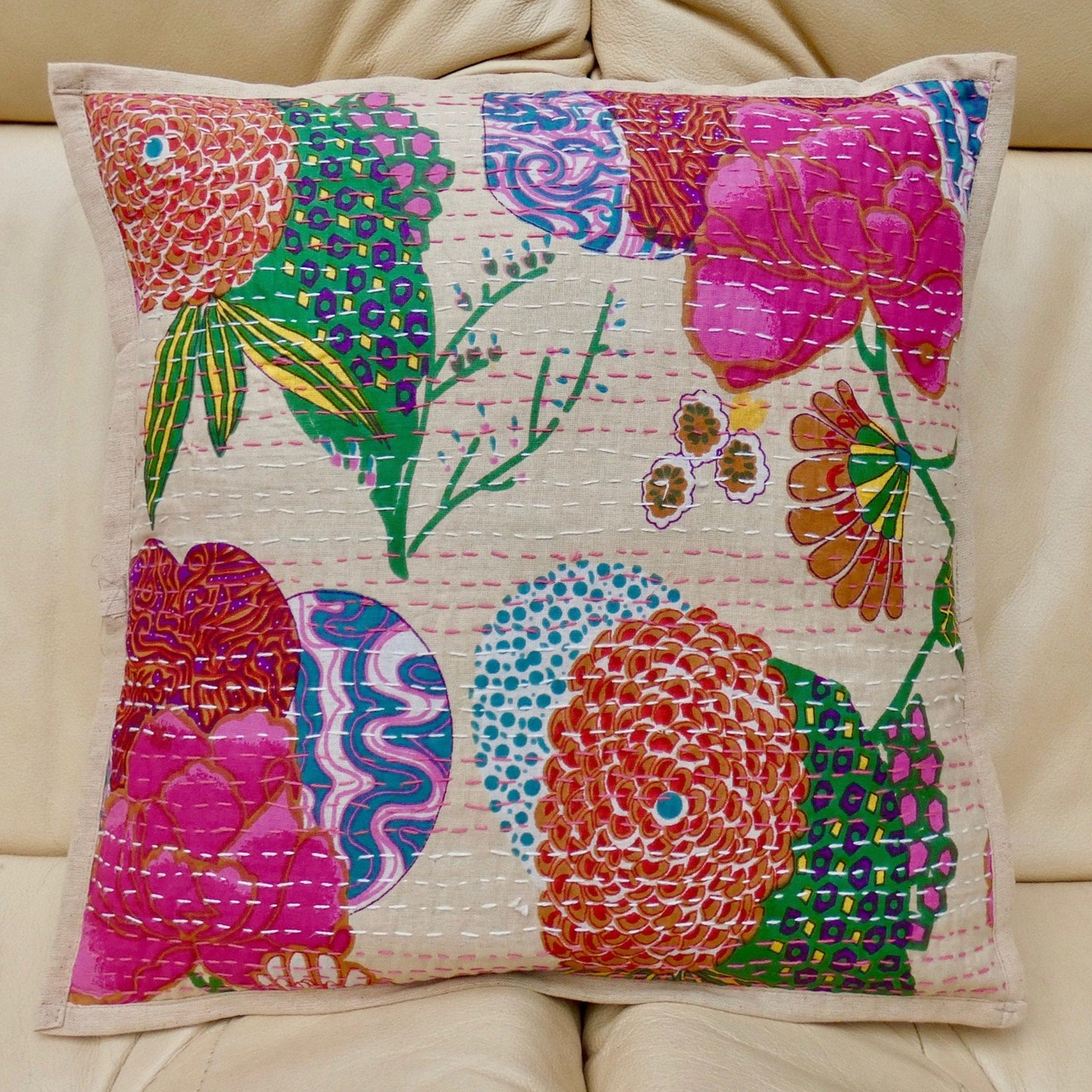 A beige cushion cover with a colorful floral design and traditional Kantha hand stitching, displayed on a sofa.