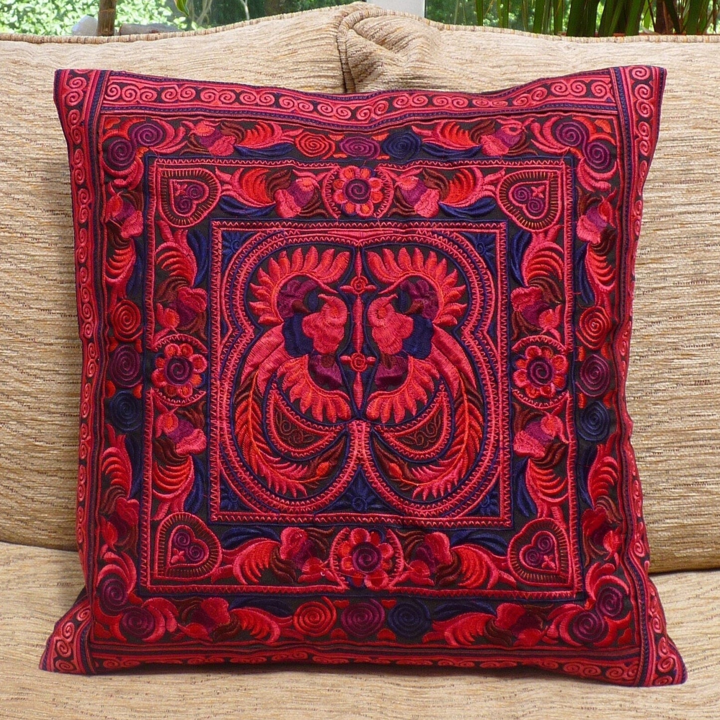 A red embroidered cushion cover with a black zip-up backing, featuring a traditional bohemian design, placed on a beige sofa cushion.