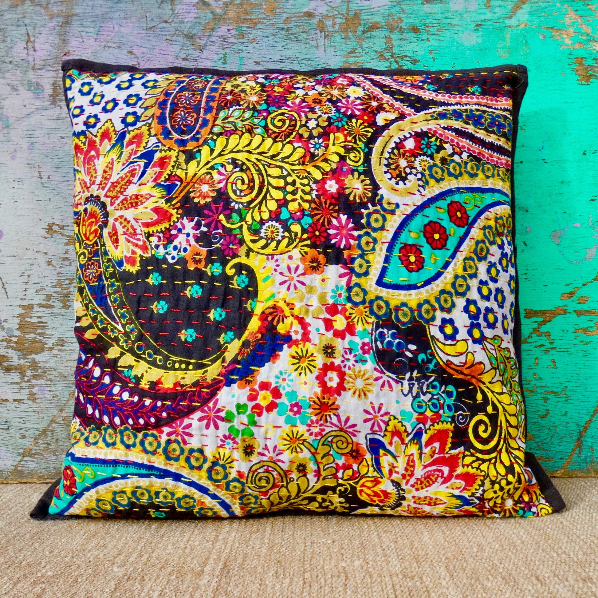 A colorful, hand-stitched cushion cover with a floral design and traditional Kantha patterns, displayed against a turquoise background.