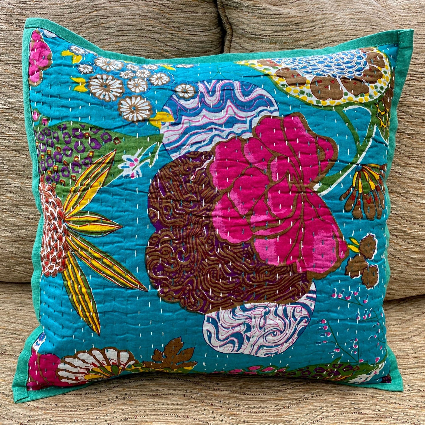 A hand stitched Kantha cushion cover with a printed floral design, featuring a vibrant turquoise background and traditional Kantha work.