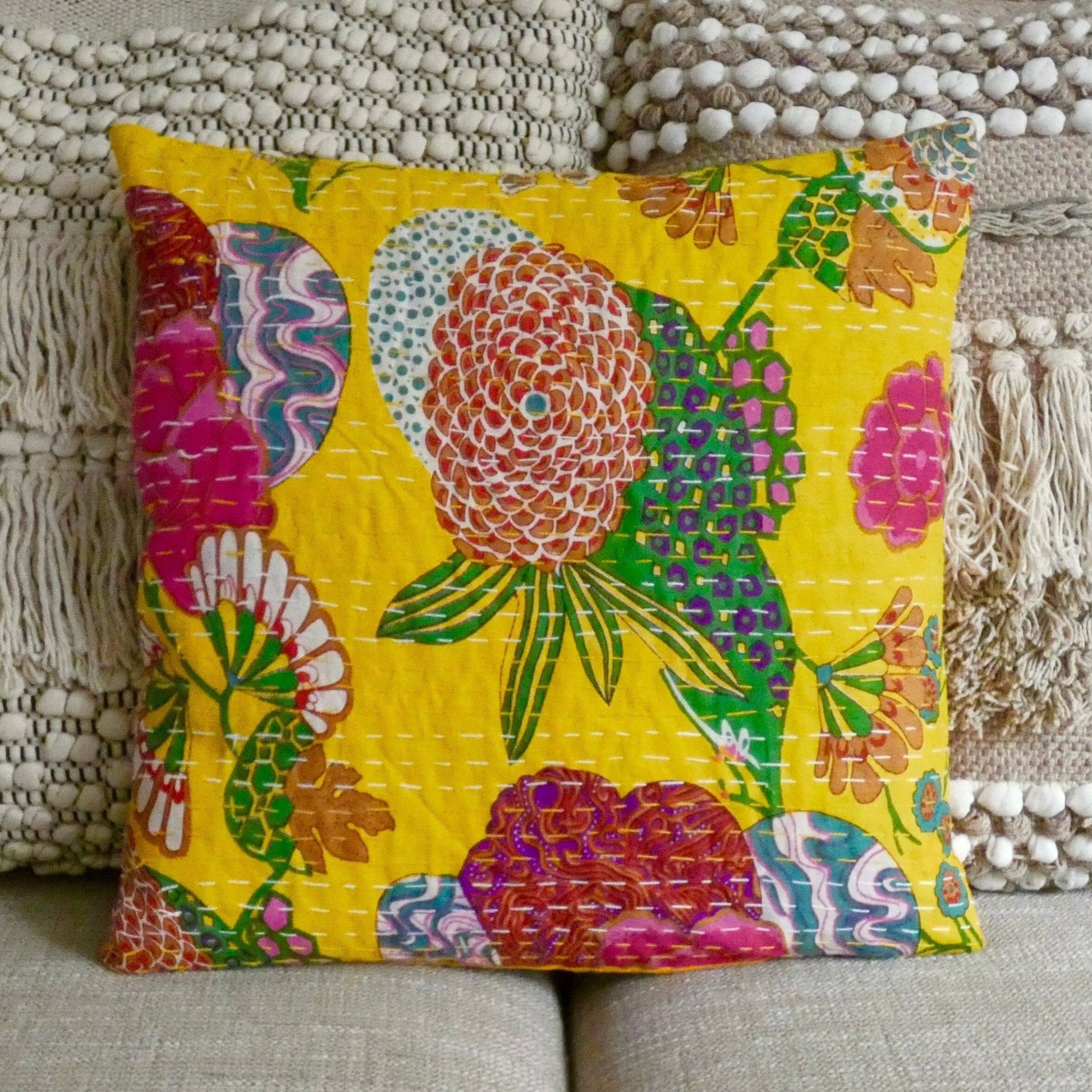 A colorful floral cushion cover with traditional Kantha design, displayed on a sofa cushion.