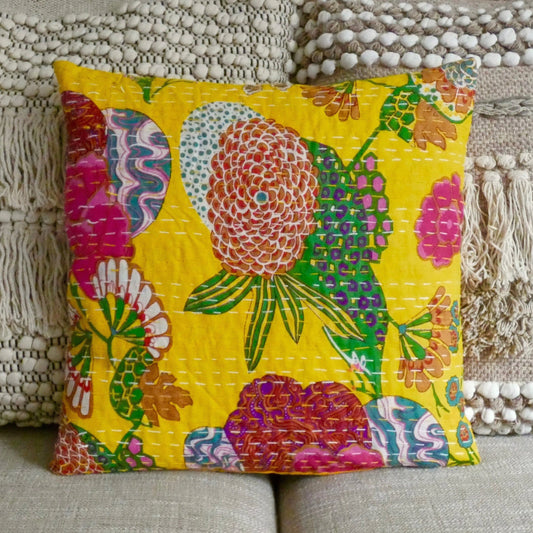 A colorful floral cushion cover with traditional Kantha design, displayed on a sofa cushion.