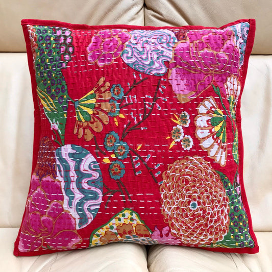 A colorful hand stitched Kantha cushion cover with a floral design on a red background, displayed on a sofa.