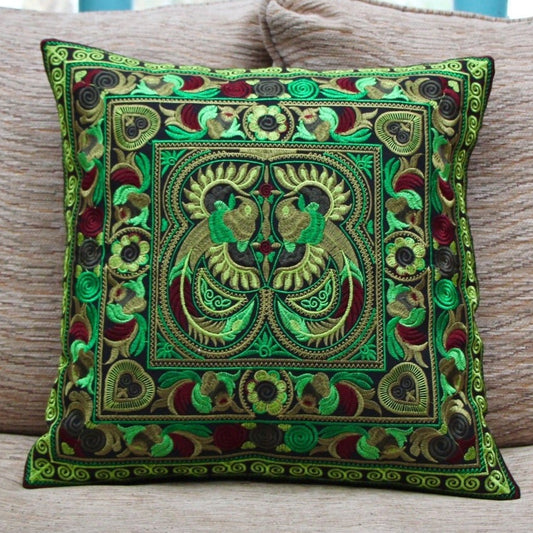 A vibrant green embroidered cushion cover with Hmong hilltribe design, displayed on a sofa with a neutral color scheme.