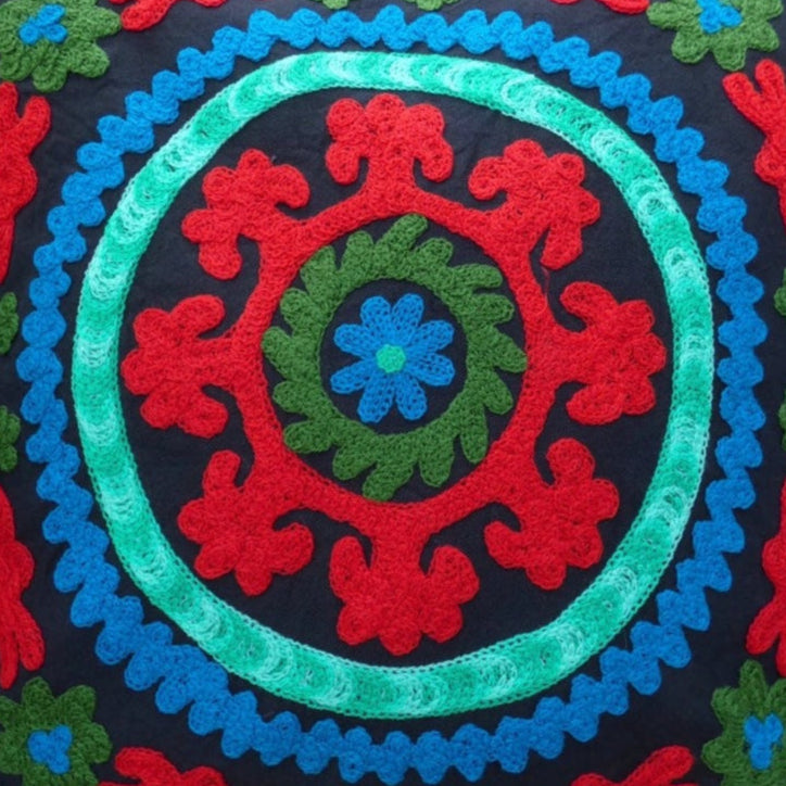 A colorful geometric patterned cushion cover with pom pom trim on a wooden chair.