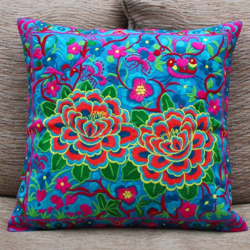 A vibrant, multicolored cushion cover with floral embroidery, displayed on a neutral sofa.