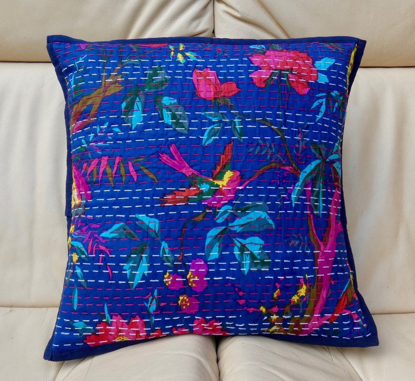 A colorful floral cushion cover with traditional Kantha design, displayed on a sofa.