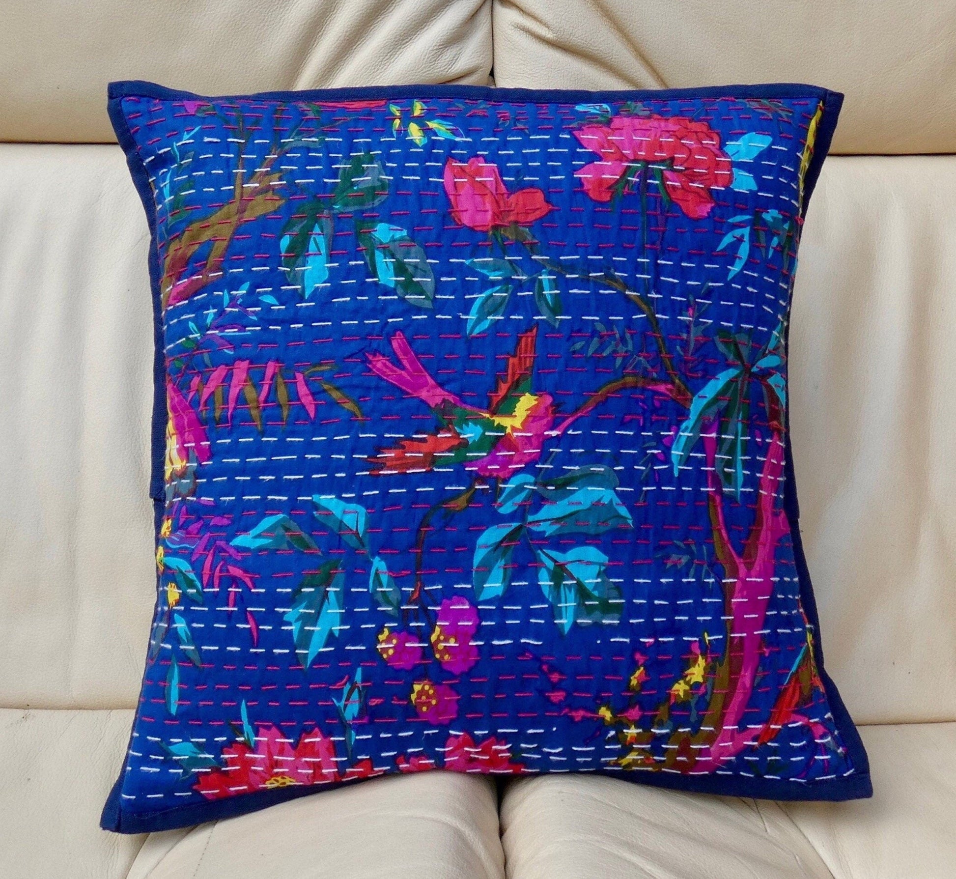 A colorful floral cushion cover with traditional Kantha design, displayed on a sofa.