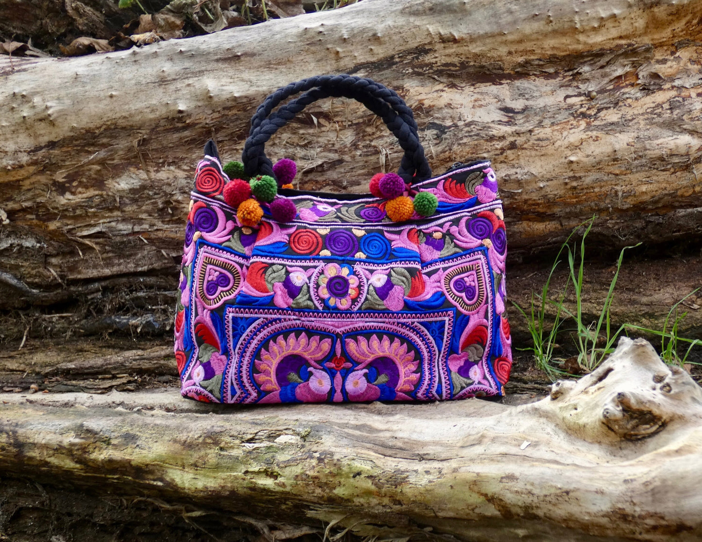 A colorful embroidered Hmong bag with decorative pompoms displayed on a wooden surface.